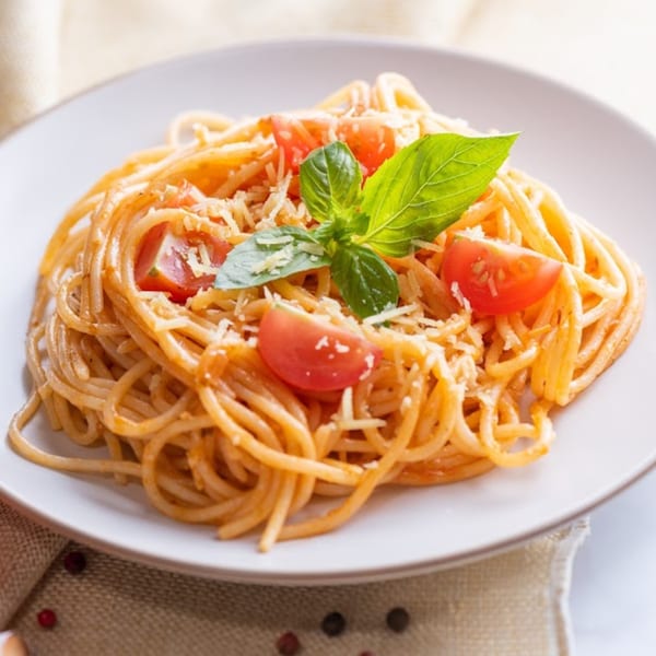 Romio's spaghetti with tomato sauce, cherry tomatoes, grated cheese, and fresh basil on a white plate.