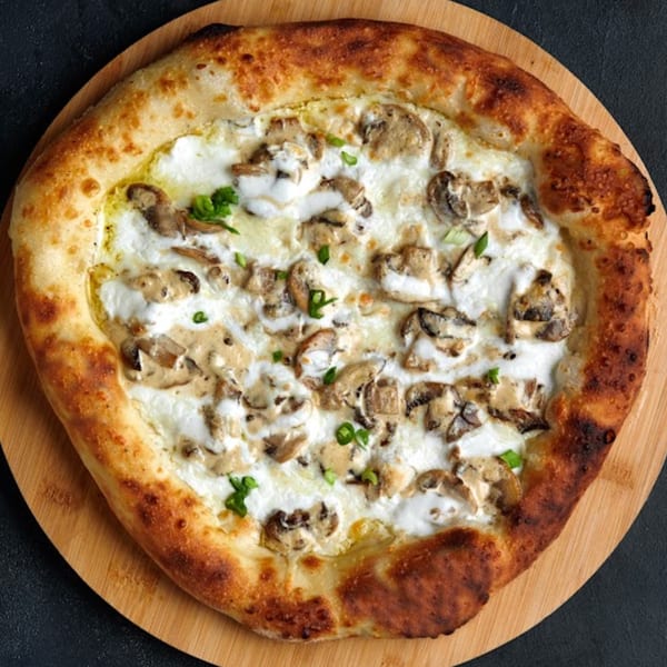 Romio's white sauce pizza with mushrooms and green herbs on a wooden board.