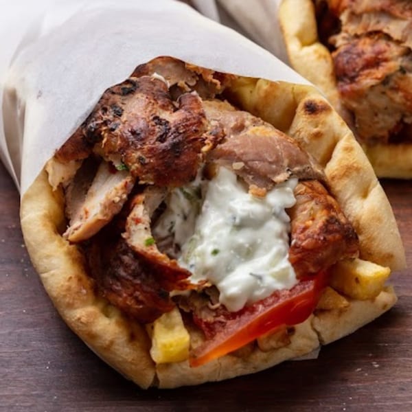 A chicken gyro with tzatziki sauce, tomatoes, and fries wrapped in pita bread.